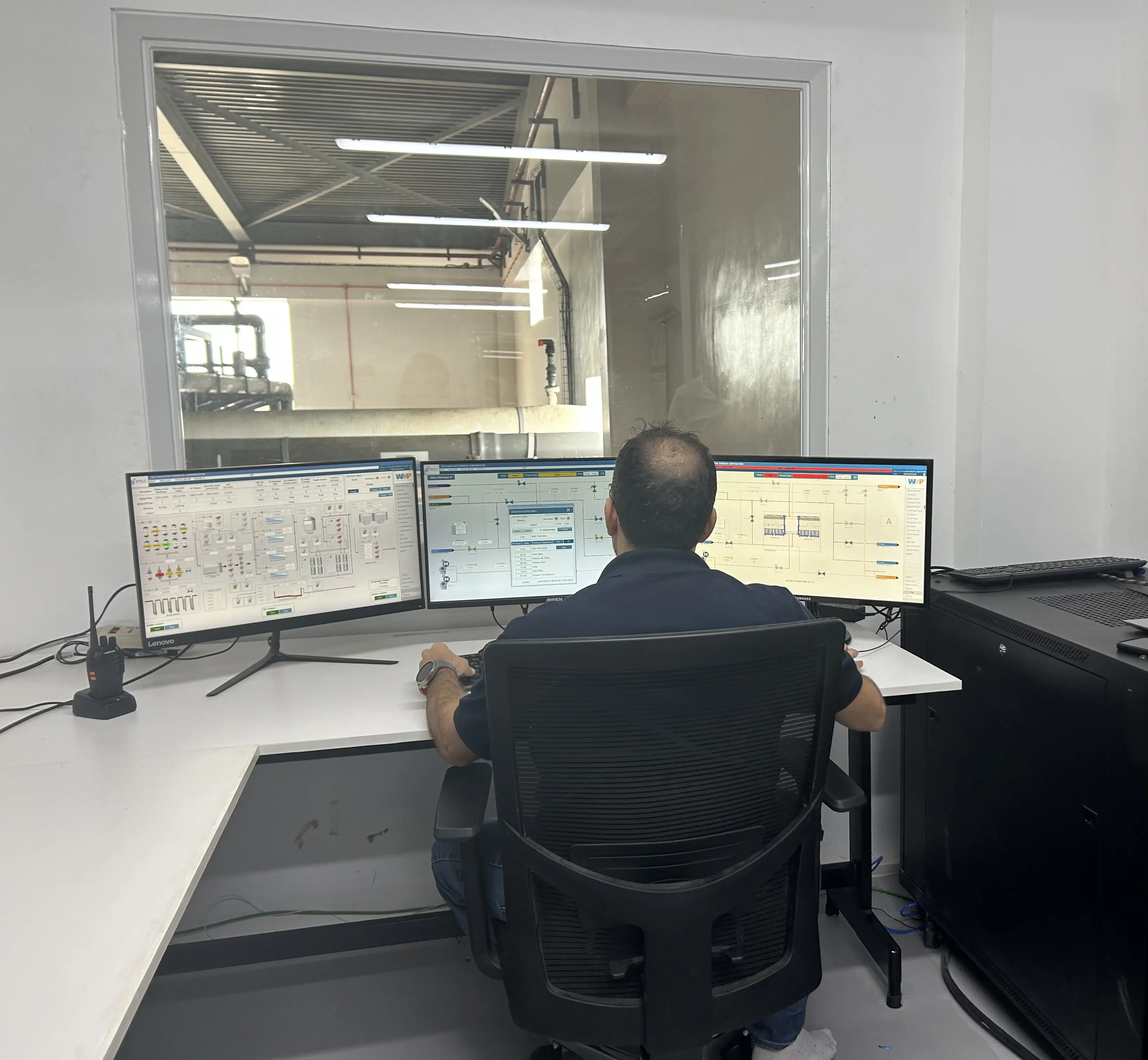 Worker looking at the computer screen in front of him with three screens showing different water treatment processes.
